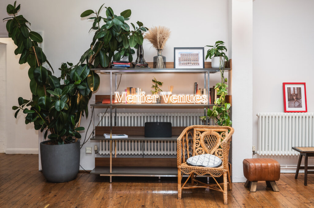 Menier Venues neon logo display surrounded by plants and modern decor