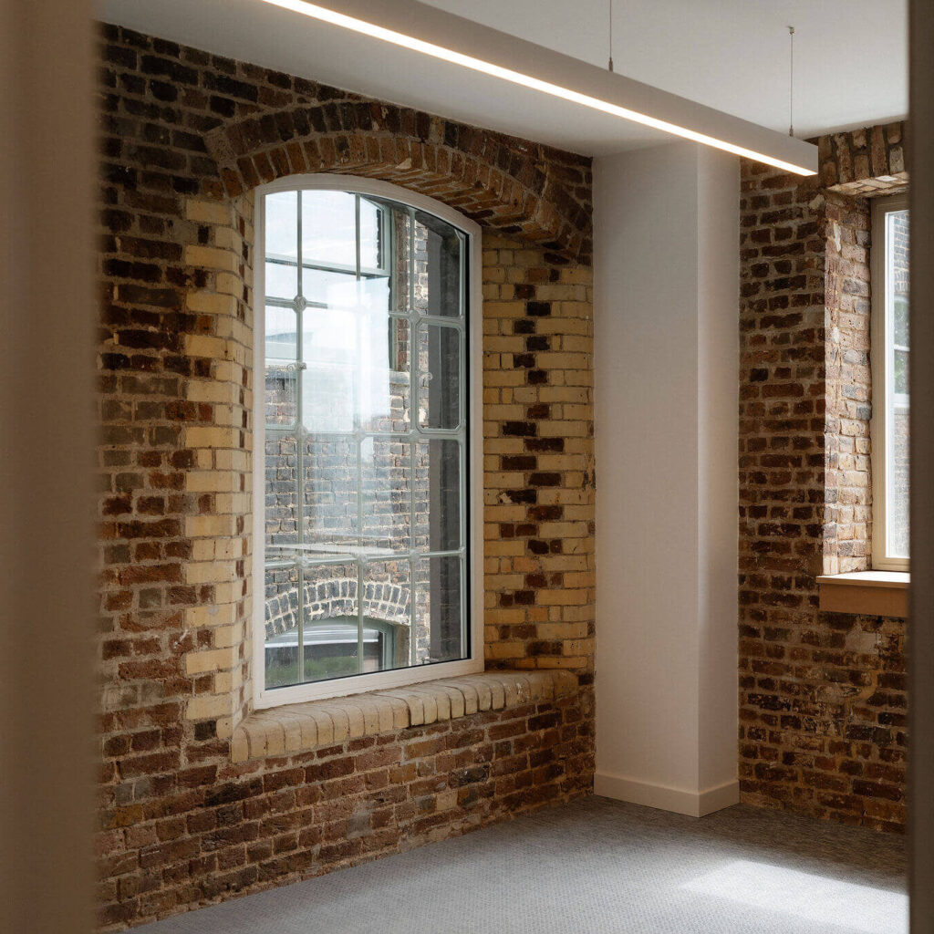 Interior office space at Menier with exposed brick walls and large arched window
