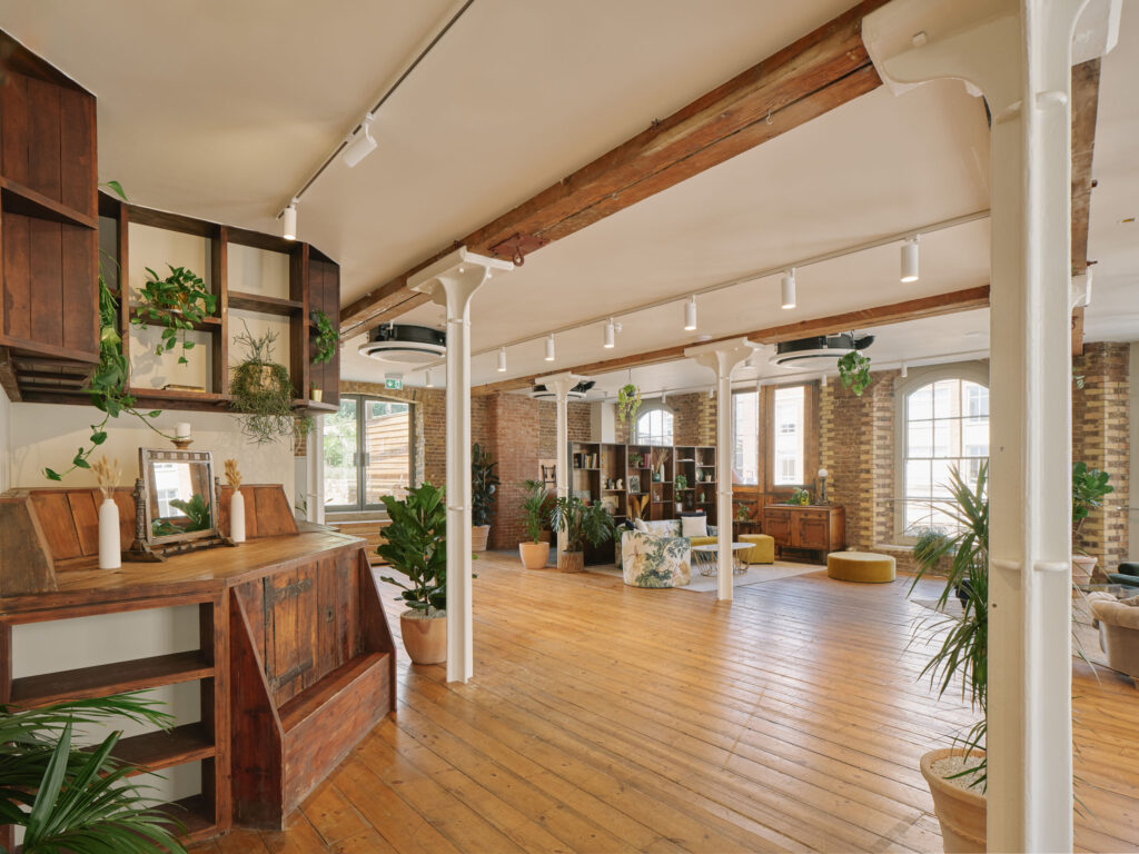 Open-plan event space at Menier Venues featuring exposed brick walls, polished wooden floors, white pillars, and modern decor with plants and seating areas