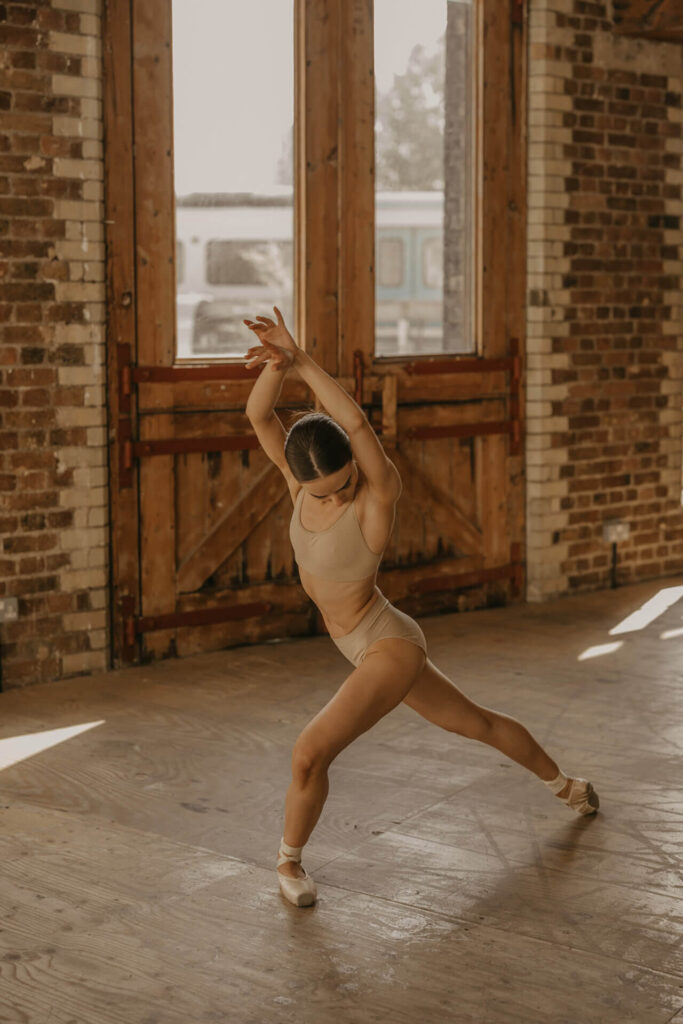 A ballet dancer in a nude leotard poses in the middle of the Menier Room