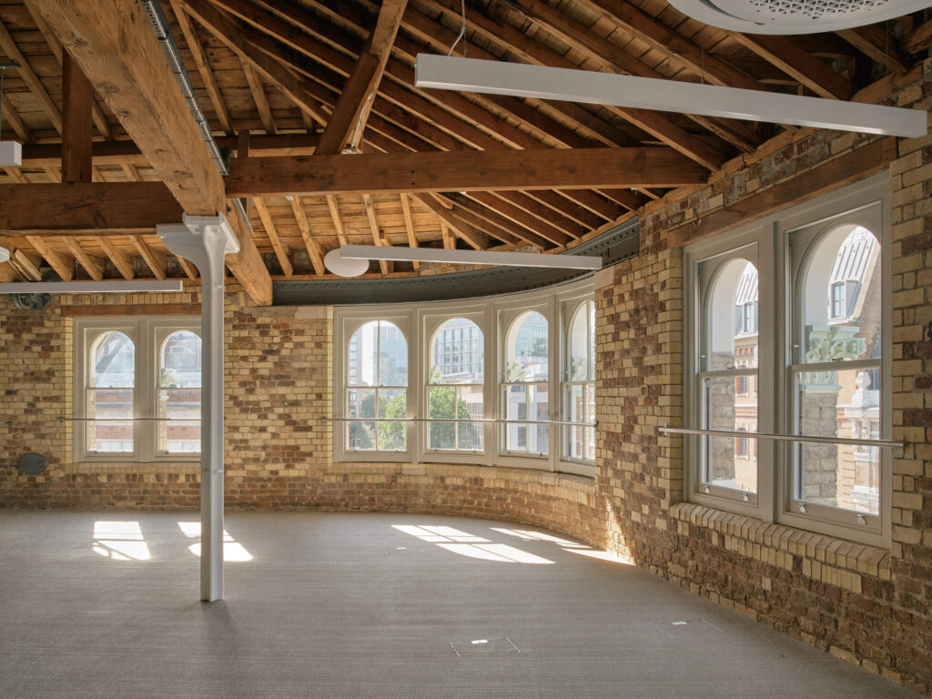 Office space with arched window, exposed brick, and ceiling beams