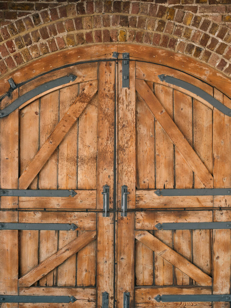 Close-up of rustic wooden double doors with iron fittings and arched brick at Menier