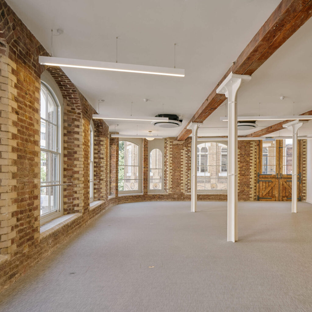 Exposed brick office space with arched window and wooden beams at Menier
