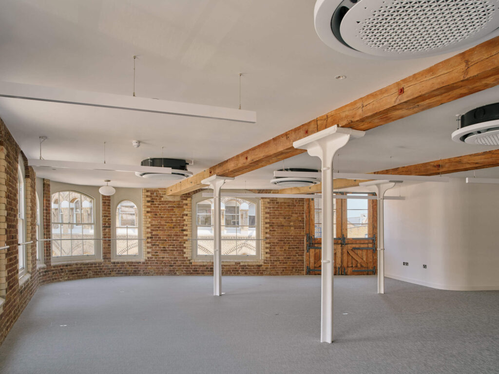 Heritage office space with arched windows, exposed brick, and ceiling beams at Menier