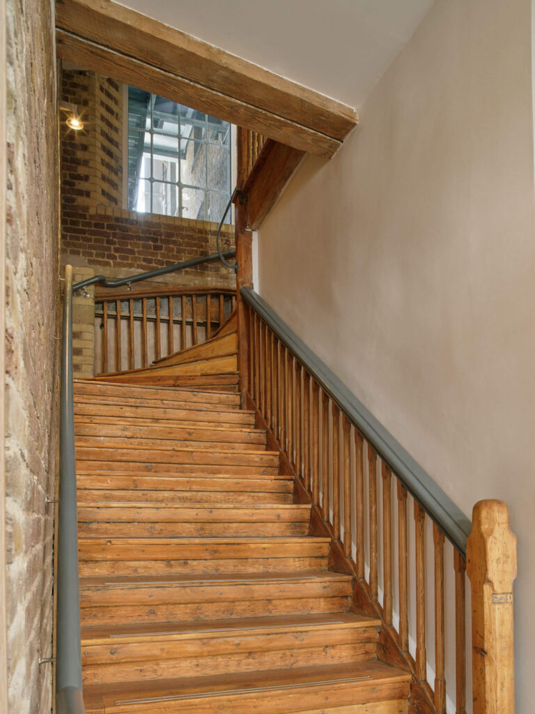 Heritage staircase with timber treads, brick wall, and window detail at Menier