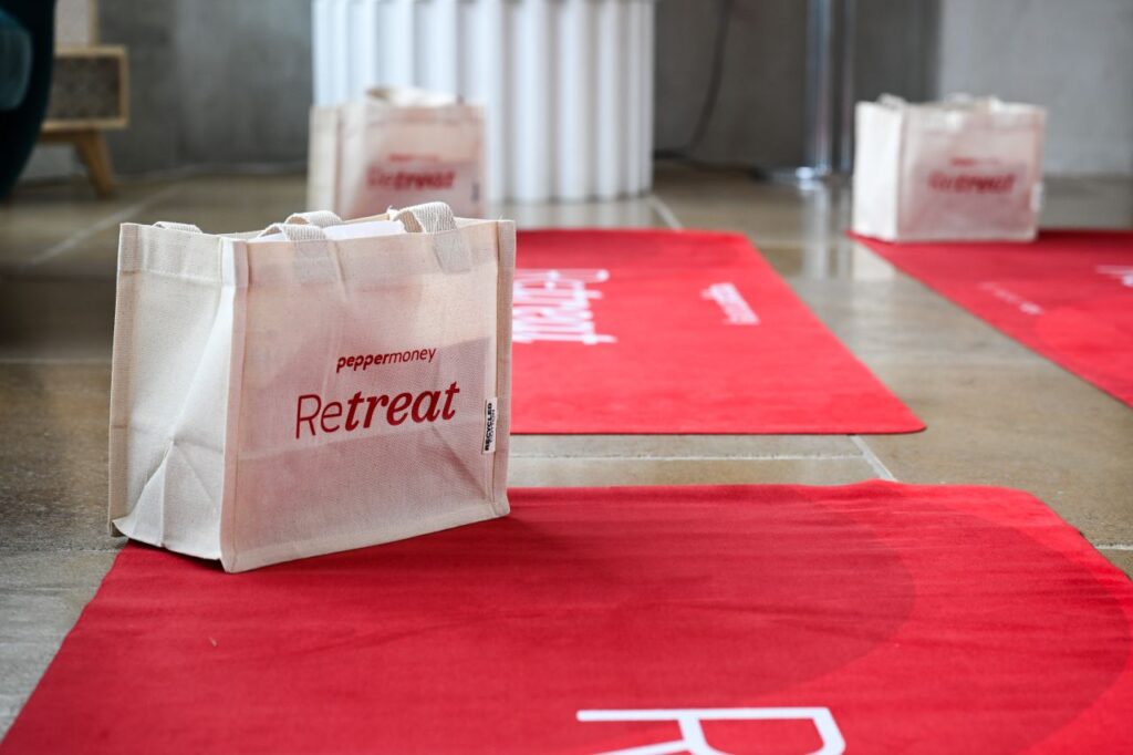 Red Pepper Money branded yoga mats and white canvas gift bags set up on a studio floor for a corporate wellness event.