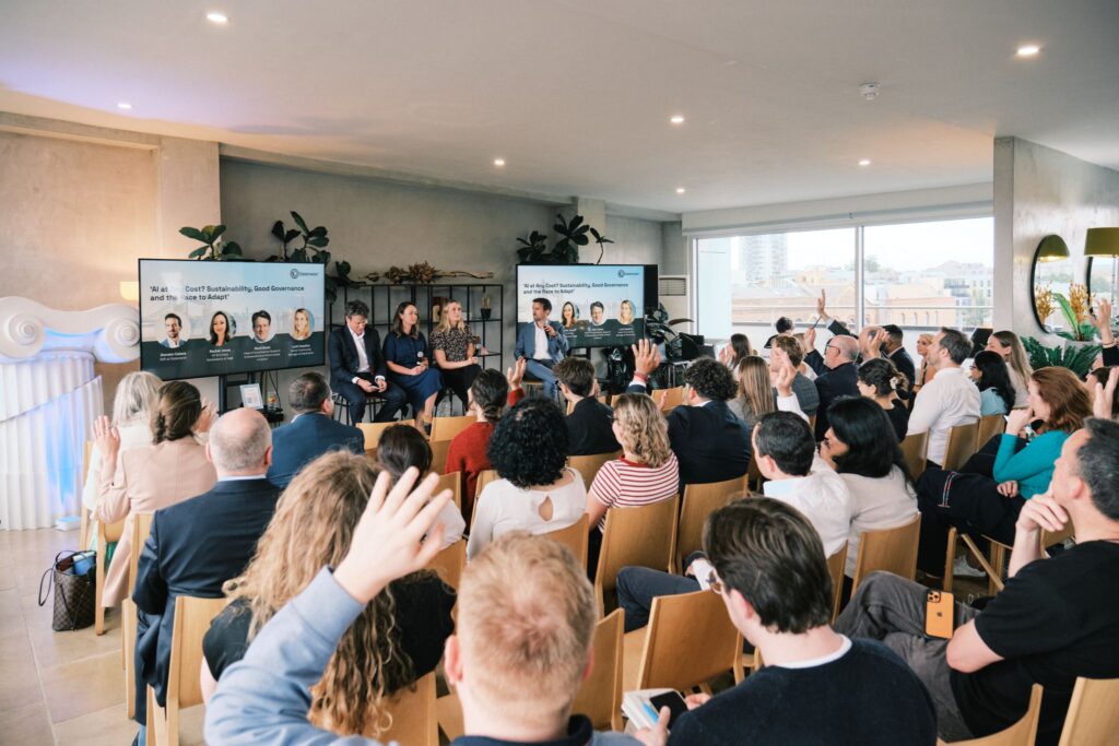 Audience members raising hands to ask questions during a panel presentation hosted in a bright penthouse event space.