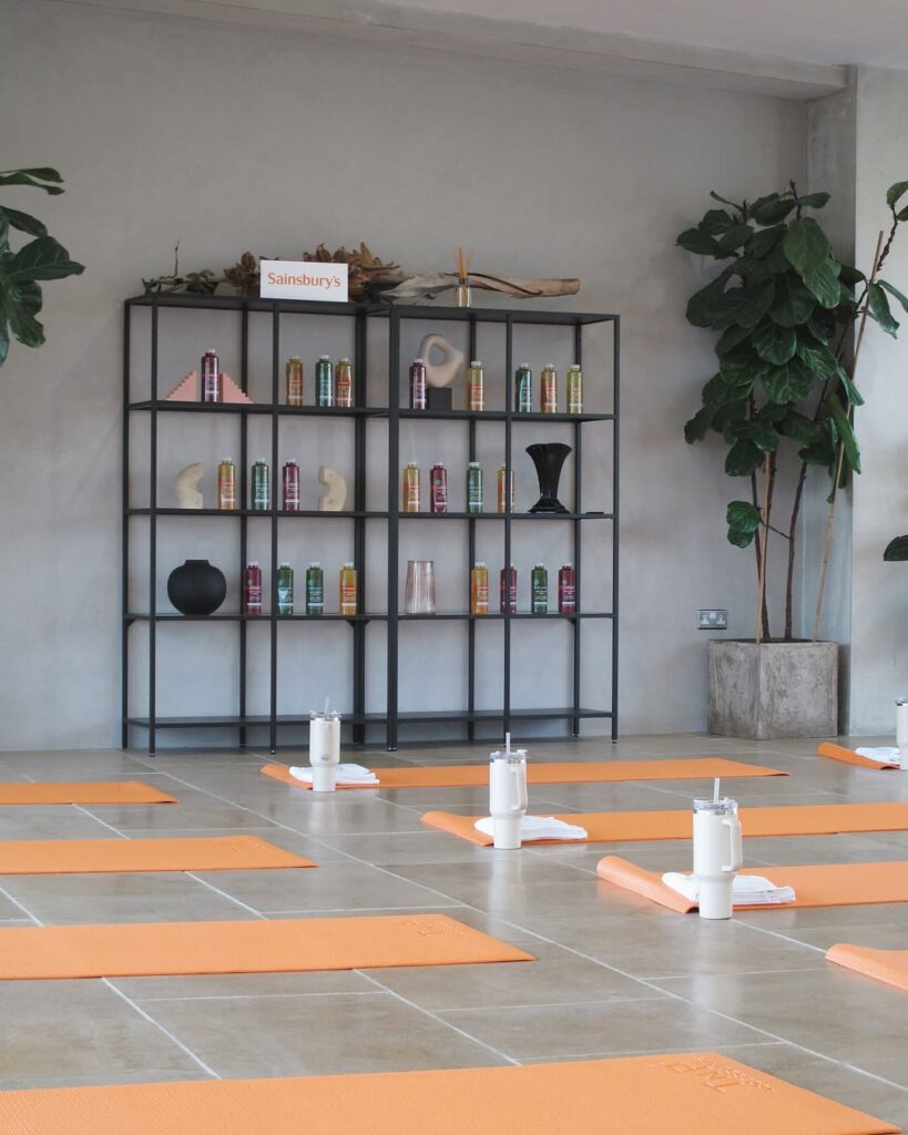 Studio floor set up with orange yoga mats, white towels, and water tumblers in front of product display shelves.